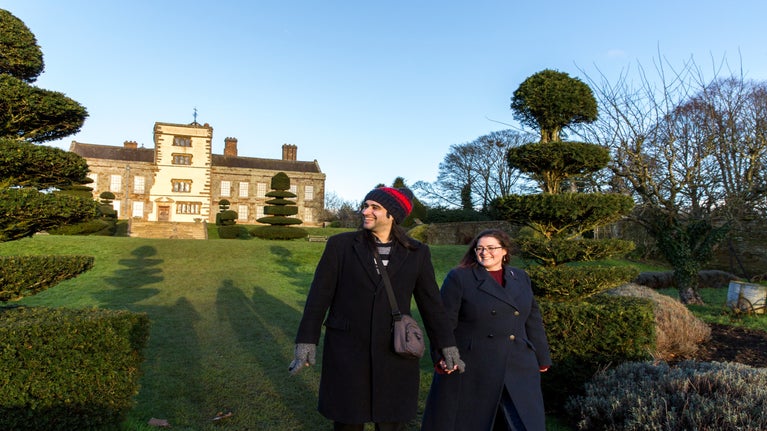Visitors in the garden at sunset at Canons Ashby, Northamptonshire. Two people hold hands in the foreground. The house at Canons Ashby in the background.
